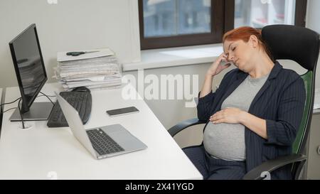 Donna incinta che dorme alla sua scrivania in ufficio. Foto Stock