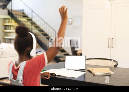 La ragazza afroamericana con le cuffie alza la mano nella lezione online basata su tablet, copia spazio Foto Stock