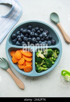 Ciotola in plastica per bambini con broccoli, mirtilli e carote. Alimenti sani per bambini nel recipiente Foto Stock