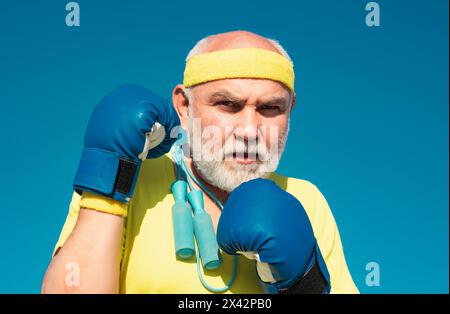 Pugilato uomo anziano - primo piano ritratto. Bell'uomo anziano che pratica i calci di boxe. Uomo sportivo anziano che indossa guanti da boxe. Divertente uomo bearded in piedi Foto Stock