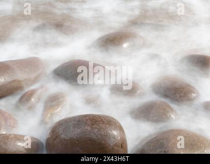 Irlanda, Kinard. Primo piano dell'onda sulle rocce lisce della spiaggia. Foto Stock