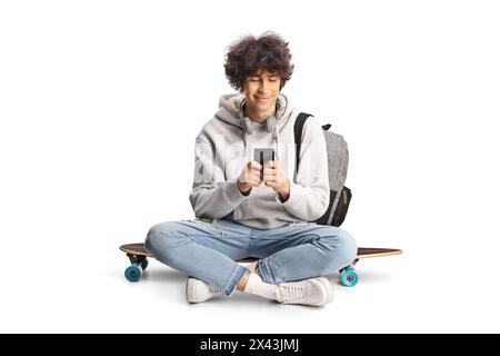 Studente maschile con uno zaino seduto su uno skateboard e che utilizza uno smartphone isolato su sfondo bianco Foto Stock