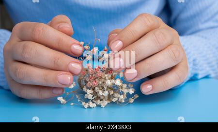 Unghie pastello morbide e curate su sfondo blu. Donna che mostra la sua nuova manicure nei colori della tavolozza pastello. Decorazioni semplici, fresche vibrazioni primaverili dai colori naturali Foto Stock