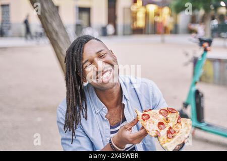 uomo con una bocca piena di pizza sorridente. fast food da mangiare per strada. Foto Stock