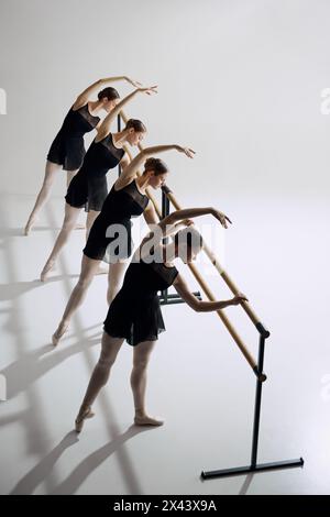 Simmetria e grazia nel balletto. Quattro ragazze flessibili, ballerine di balletto in piedi a barre e si allenano su sfondo grigio in studio Foto Stock