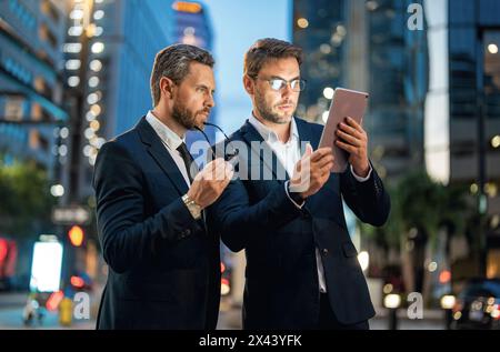 Affari notturni in città. Gli uomini d'affari controllano le loro e-mail e esaminano documenti importanti su tablet durante la notte in città. Affari, tecnologia e persone Foto Stock