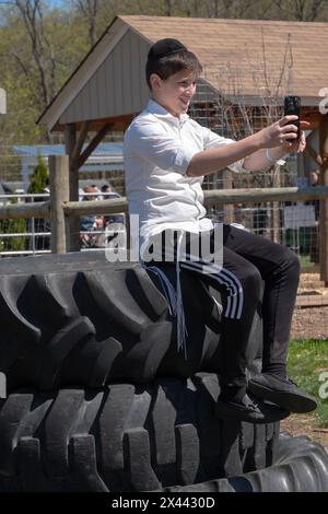 Un adolescente ebreo ortodosso scatta un selfie mentre si siede su una pila di pneumatici di grandi dimensioni. In una fattoria nella contea di Rockland e durante Pesach 2024. Foto Stock