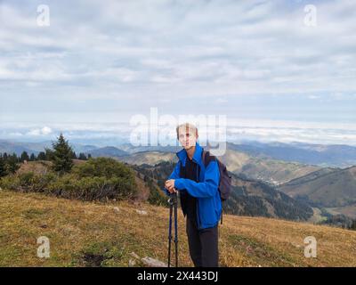 Giovane escursionista maschile con pali da trekking e zaino in piedi su una cresta di montagna. Foto Stock