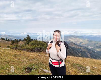 Donna sorridente escursionista con uno zaino in piedi su una montagna che si affaccia su colline lontane. Foto Stock