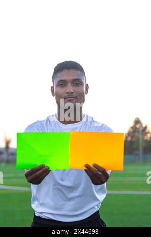 Arbitro di calcio latino che prende due carte sul campo. Vista frontale dell'arbitro di calcio che prende le carte Foto Stock