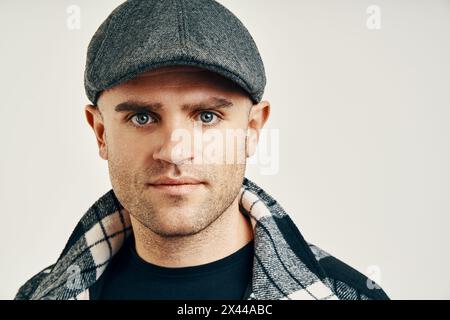 Uomo alla moda con cappello in tweed su morbido sfondo bianco e spazio per le copie. Ispirazione in stile Peaky Blinders Foto Stock