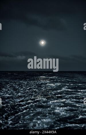 Luna piena nel cielo sopra il mare di notte durante il tempo tempestoso Foto Stock