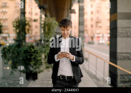 Giovane donna d'affari che usa il telefono cellulare mentre cammina sul marciapiede Foto Stock
