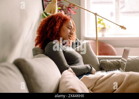 Vista laterale di una giovane donna d'affari con laptop seduto sul divano nel soggiorno Foto Stock