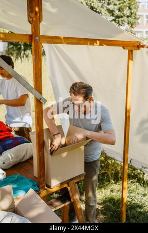 Volontario maschile senior che organizza abiti in una scatola di cartone sul tavolo durante un viaggio di beneficenza presso il centro della comunità Foto Stock