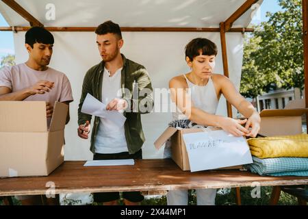 Gruppo di volontari maschi e femmine che attaccano le targhette dei nomi sulle scatole durante un viaggio di beneficenza presso il centro della comunità Foto Stock