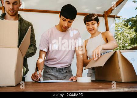 Visione a basso angolo di una volontaria che assiste un collega maschio durante la preparazione delle etichette dei nomi durante la campagna di beneficenza presso la comunità Foto Stock