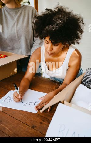 Giovane donna volontaria con capelli ricci che fanno i nomi tag mentre si appoggia sul tavolo del centro della comunità Foto Stock