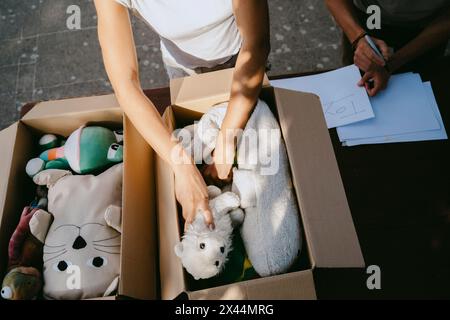 Vista ad alto angolo di una volontaria che confeziona giocattoli imbottiti in scatole presso il centro della comunità Foto Stock