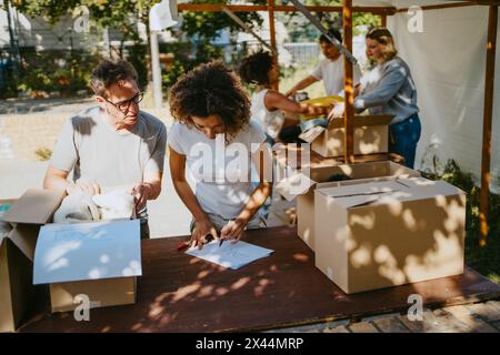 Volontario di sesso maschile che assiste una collega mentre si etichettano le scatole sul tavolo durante l'attività benefica presso il centro comunitario Foto Stock