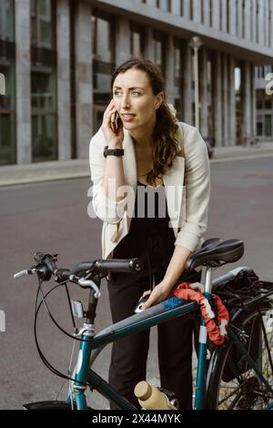 Donna d'affari che blocca la bicicletta mentre parla con uno smartphone in città Foto Stock