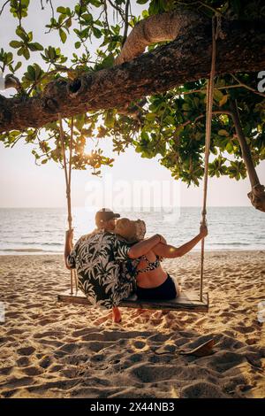 Vista posteriore di una romantica coppia anziana che guarda il mare seduto sull'altalena Foto Stock