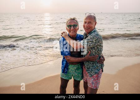 Ritratto di una coppia gay sorridente che si abbraccia a vicenda mentre si trova vicino alla spiaggia Foto Stock