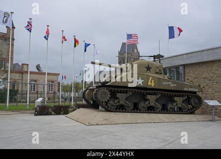 Sainte-Mere-Eglise, Francia - 19 aprile 2024: Museo aereo a Sainte-Mere-Eglise. Carro armato Sherman. Chiesa sullo sfondo. Stile di vita nell'area urbana. Clo Foto Stock