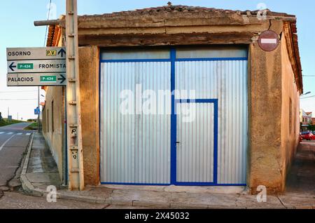 Vecchio fienile con nuove porte in metallo su un angolo in un incrocio con cartelli stradali in luce serale Lantadilla Palencia Castiglia e Leon Spain Foto Stock