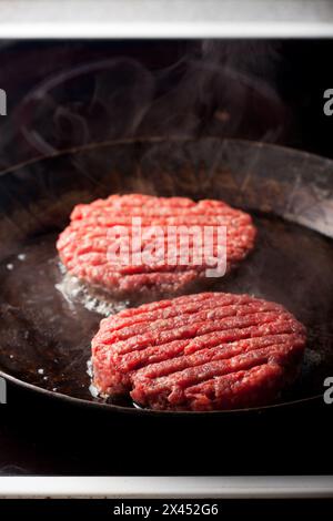 Due polpette di carne di manzo in una padella di ferro Foto Stock