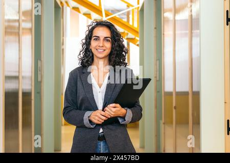 Ritratto di una donna sorridente che guarda la fotocamera che tiene la cartella in un ufficio moderno Foto Stock