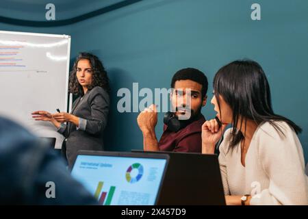 Donna d'affari che conduce una riunione che analizza i dati aziendali insieme ai colleghi in un moderno spazio di coworking Foto Stock