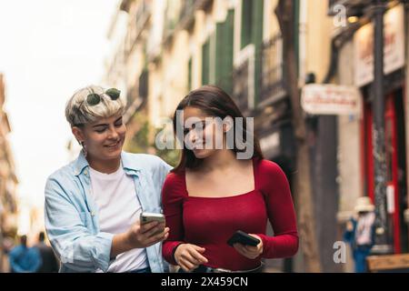 due ragazze adolescenti che camminano e guardano qualcosa ai suoi cellulari Foto Stock