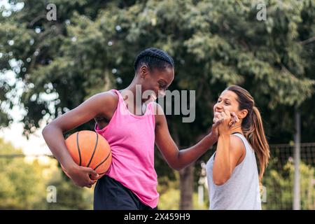 Giovani atlete che giocano a basket in abbigliamento sportivo su un campo urbano della città. Si divertono e si divertono a cinque in alto mentre si divertono. Foto Stock