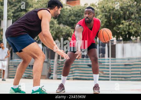 Giovani atleti che giocano a basket in abbigliamento sportivo su un campo urbano della città Foto Stock