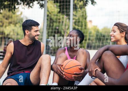Team Bonding: Amici seduti sul campo da pallacanestro, chiacchierando e festeggiando dopo una partita Foto Stock
