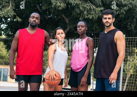 Ritratto di un gruppo multirazziale in abbigliamento sportivo che gioca a basket. Guardano la fotocamera con sicurezza e sorridono Foto Stock