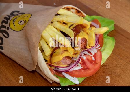 Tortilla saporita con salsicce salate, patatine fritte, insalata verde, pomodori, cipolle, e cavolo, tutto confezionato per un pasto da asporto Foto Stock