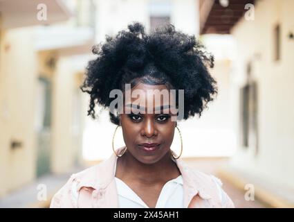 Ritratto di una bella donna nera con i capelli afro che guarda la fotocamera. Ha alcune caratteristiche caratteristiche e sembra sicura di sé. Foto Stock