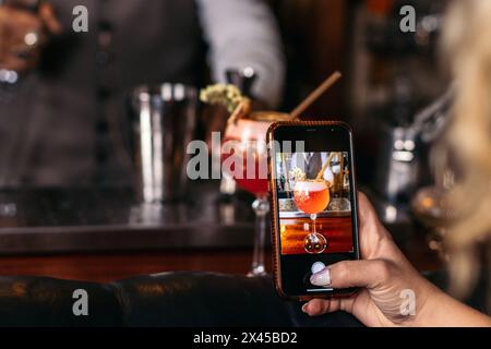 Primo piano di una donna irriconoscibile che scatta foto con lo smartphone di un cocktail. Lei è una cliente in un bar Foto Stock