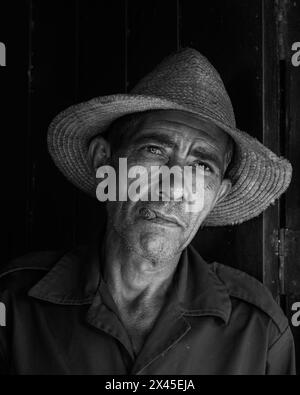 Un coltivatore di tabacco che indossa un cappello di paglia che fuma un sigaro davanti alla porta d'ingresso della sua fattoria nella Val di Vinales, Vinales, Cuba. Foto Stock
