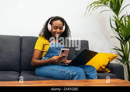 Giovane donna nera che si diverte a casa con il suo stile di vita digitale, perfetta per contenuti e marketing legati alla tecnologia Foto Stock