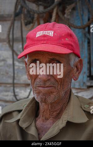 Un coltivatore di tabacco che indossa un berretto rosso in posa per la sua foto da scattare in una piantagione nella Valle di Vinales, Vinales, Cuba. Foto Stock