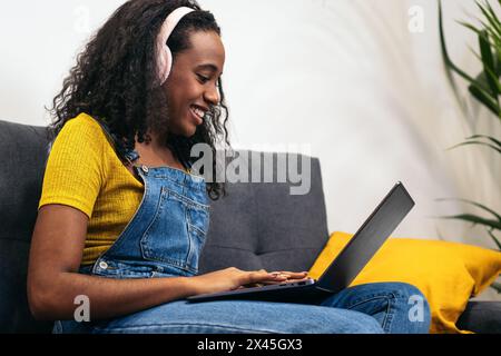 Giovane donna nera che si diverte a casa con il suo stile di vita digitale, perfetta per contenuti e marketing legati alla tecnologia Foto Stock