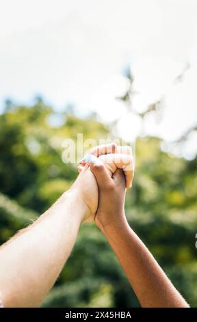 Primo piano delle mani di una coppia interrazziale che si incastrano le dita. Foto Stock