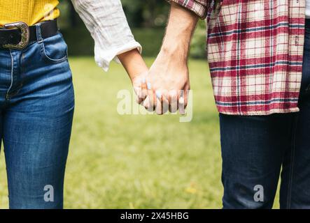 Primo piano delle mani di una coppia interrazziale che si incastrano le dita. Foto Stock
