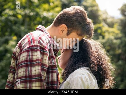 Giovane coppia interrazziale che abbraccia e bacia nel parco Foto Stock
