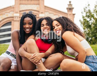 Tre ragazze afroamericane con i capelli afro sedute in un parco che si divertono. Si divertono insieme e la loro amicizia. Foto Stock