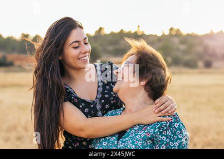Sorridente donna anziana in un bellissimo campo di girasoli al tramonto con sua nipote che si diverte insieme Foto Stock