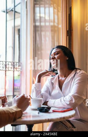 Primo piano di una bella donna latina in abiti casual sorridente mentre parla con qualcuno in un bar. Guarda il suo partner eccitato e attento Foto Stock